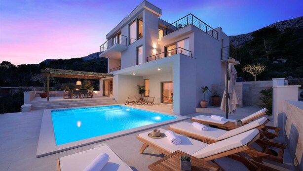 A modern two-story house with a swimming pool, outdoor seating, and a mountain backdrop.