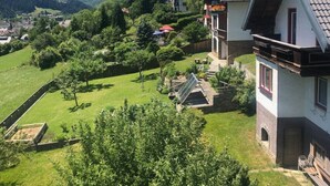 Un edificio de estilo chalete tradicional con techo inclinado, rodeado de exuberante vegetación y una vista despejada de montañas distantes.