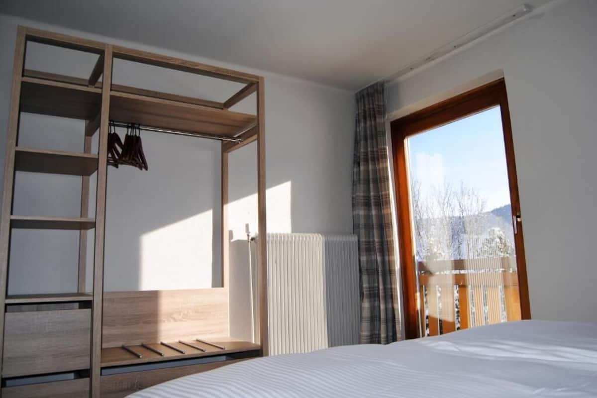 Un dormitorio con estructura de cama de madera, armario empotrado y vistas a un balcón.