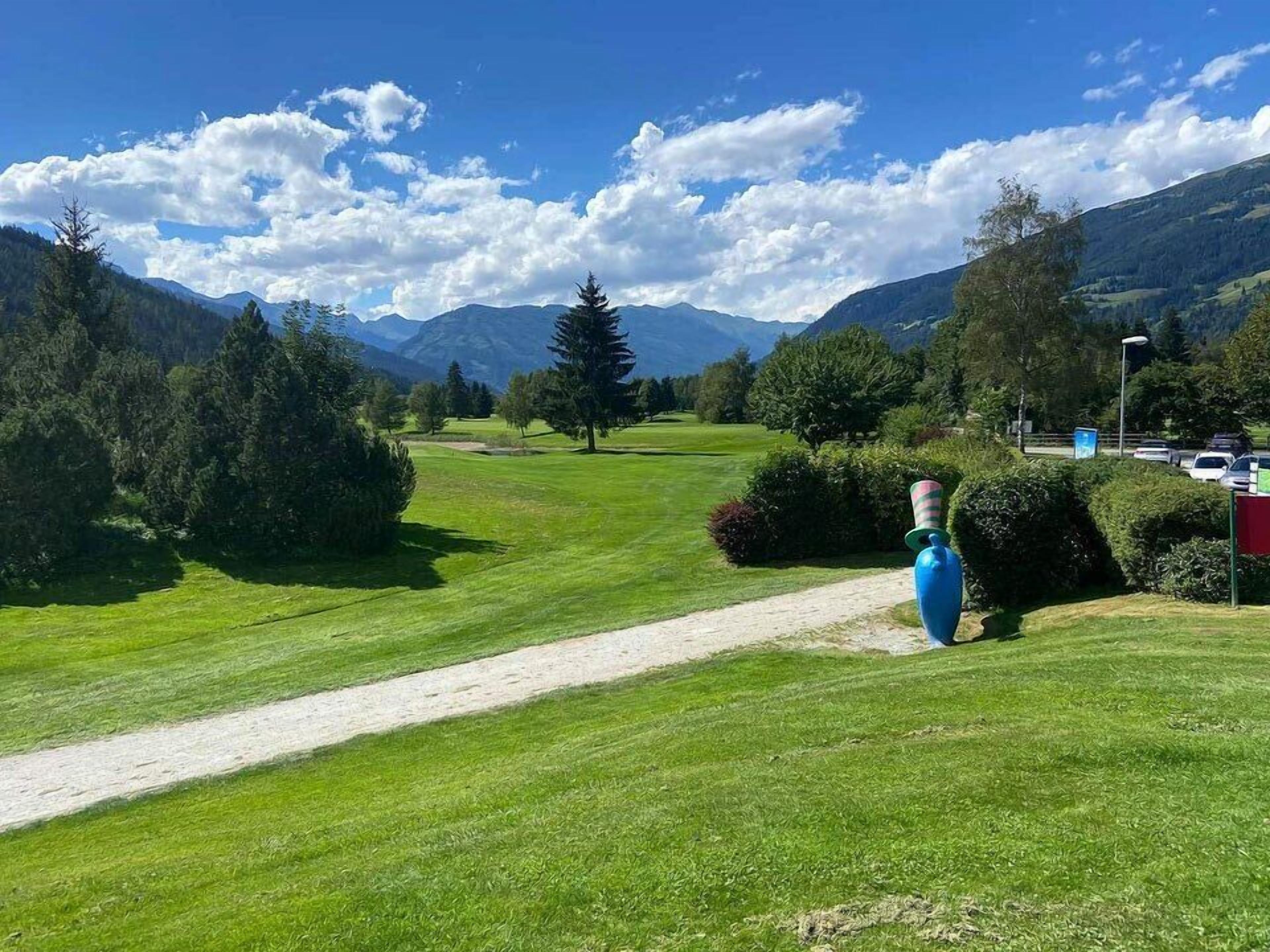 A golf course with a clear path, surrounded by trees and mountains.