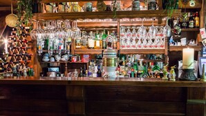 Un bar con estantes llenos de botellas y copas variadas, una barra de madera y una exhibición de objetos decorativos.