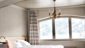 Un dormitorio con cama, una silla, una mesa y ventana con vistas a árboles.