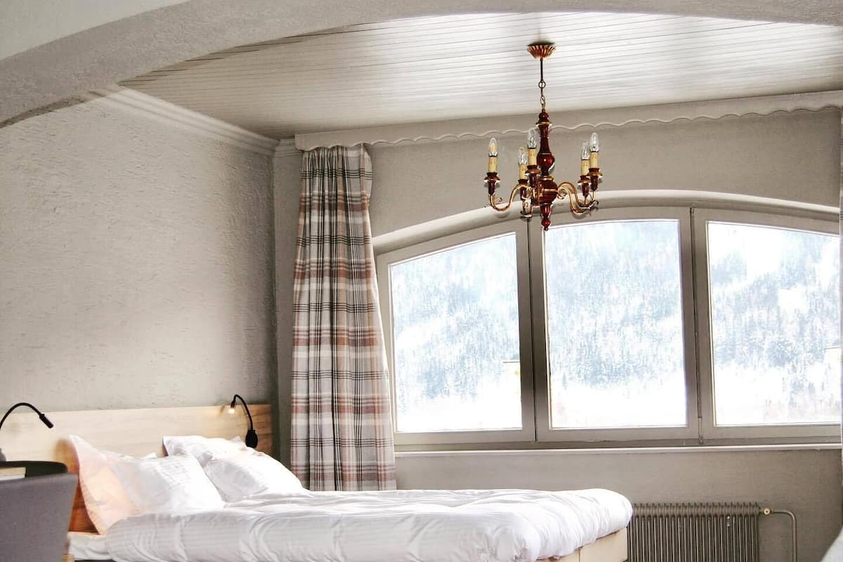 Un dormitorio con cama, una silla, una mesa y ventana con vistas a árboles.