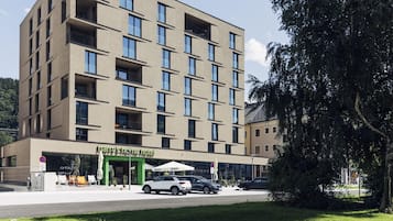 A modern hotel with a flat facade, multiple balconies, and a green entrance.