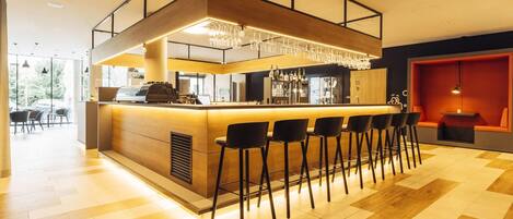 A modern bar area with a wooden counter, black bar stools, and a chandelier.