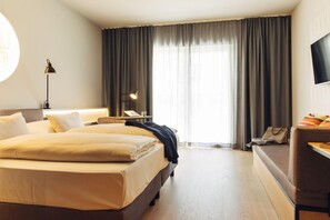 Habitación de hotel con una cama grande, un escritorio, una silla, un televisor y una ventana con cortinas.