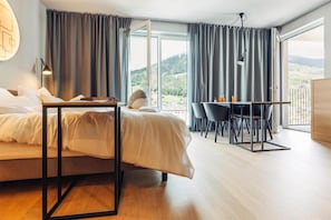A bedroom with a bed, a desk, and a view of the outdoors.