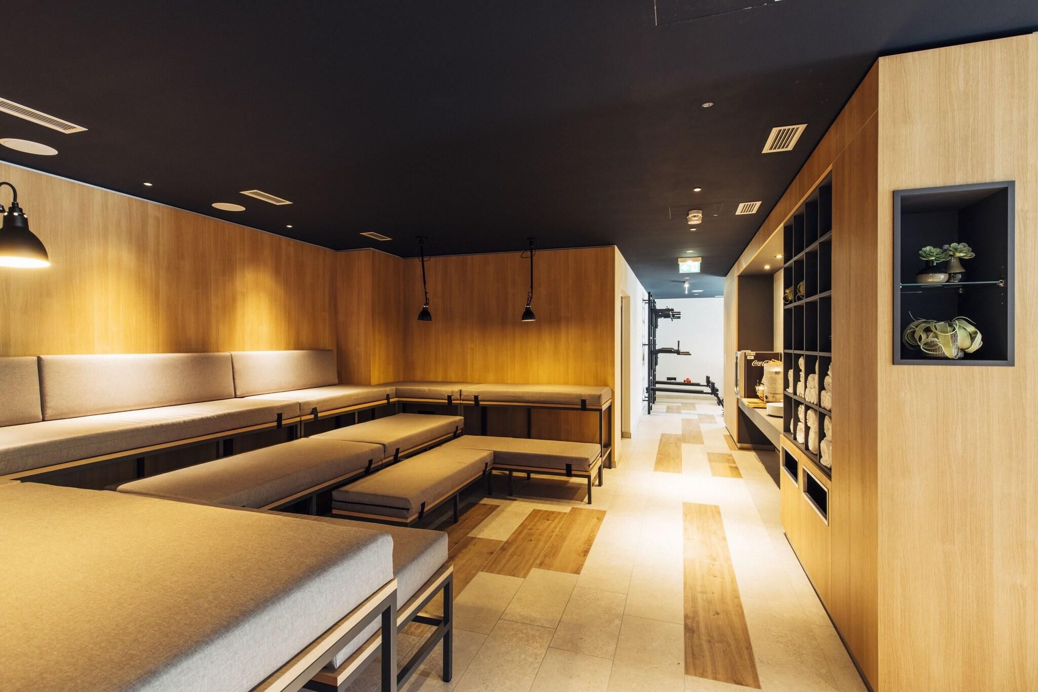 A modern interior with wooden panel walls, a central seating area with benches, pendant lighting, and a display shelf with items.
