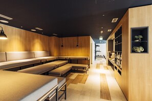 Un interior moderno con paneles de madera, una zona de estar central con bancos, iluminación colgante y un estante con objetos.