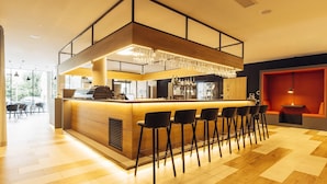 Een moderne bar met een houten toonbank, zwarte barkrukken en een kroonluchter.