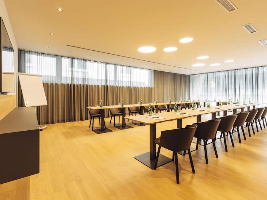 A conference room with a long table, chairs, a podium, and a large window with curtains.