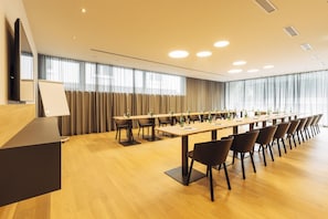 Uma sala de conferências com uma mesa comprida, cadeiras, um pódio e uma grande janela com cortinas.