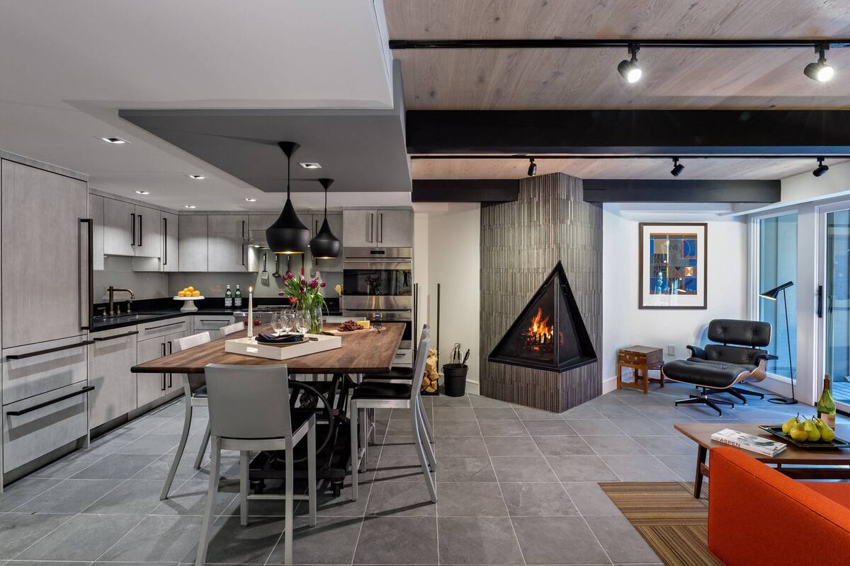 A modern kitchen with grey cabinets, a wooden dining table, and pendant lighting.
