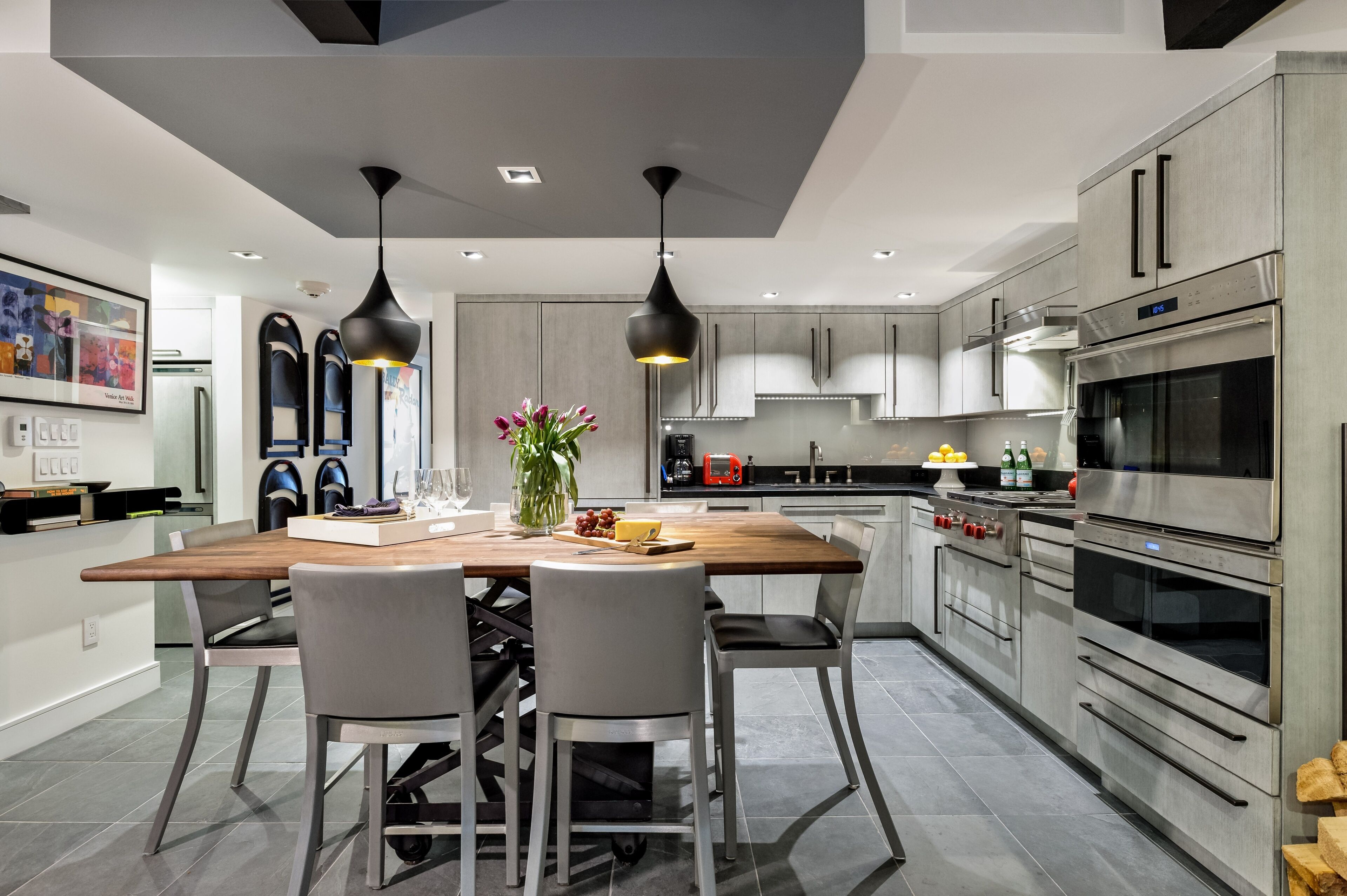 Une cuisine moderne dotée d’un îlot central, d’appareils électroménagers en acier inoxydable et de luminaires suspendus.