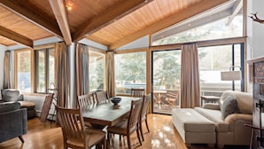 A spacious living area with a wooden dining table, comfortable seating, and large windows offering a view of the outdoors. - Deluxe 2 Bedroom Apartments at Resort with Outdoor Pool & Hot Tub (Aspen)