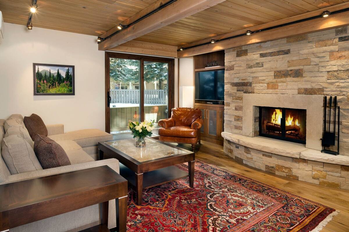 A cozy living room with a stone fireplace, a leather armchair, and a large window overlooking a deck.