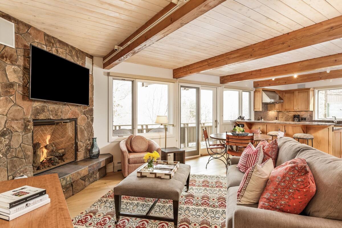 A cozy living room with a stone fireplace, a flat-screen TV, a comfortable sofa, and a dining area with a table and chairs.