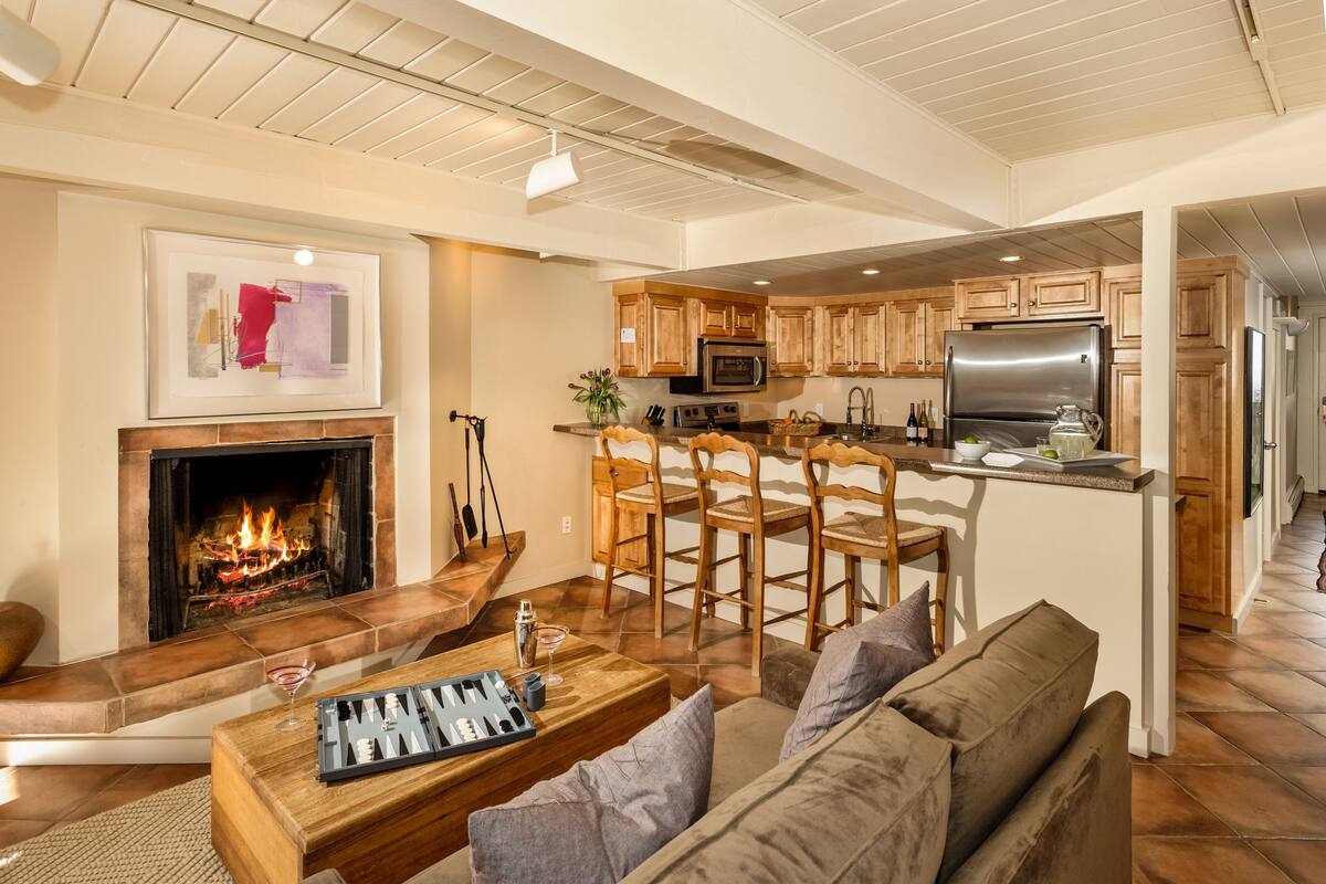 A spacious living room with a fireplace, a kitchen area with wooden cabinets, and a dining area with bar stools.