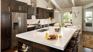 A modern kitchen with dark wooden cabinets, stainless steel appliances, and a large island with fruit and a vase. - Comfortable & Modern 2 Bedroom Apartments - Right on the Slopes! (Aspen)