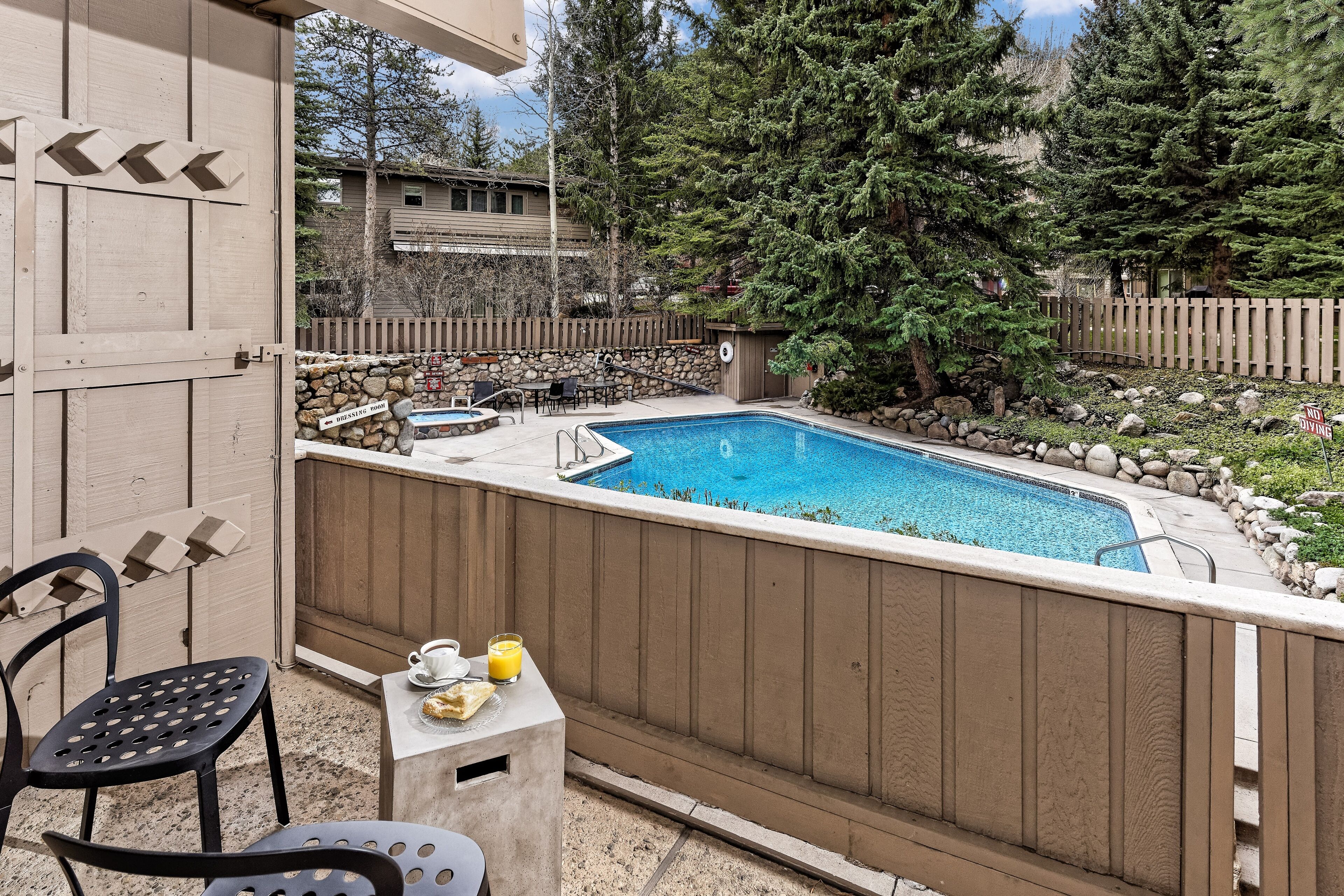 A backyard with a swimming pool, a small table with chairs, and a wooden fence.