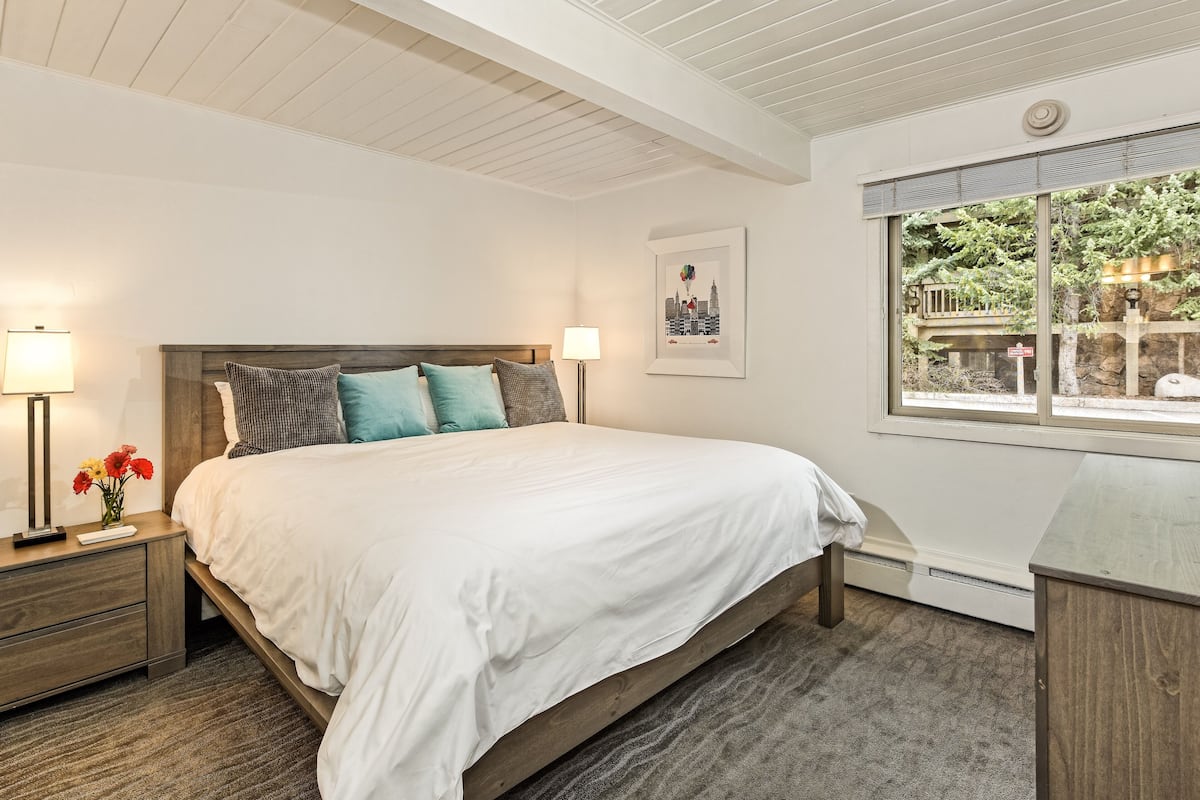 A bedroom with a bed, nightstands, a window with a view, and a wall-mounted picture.
