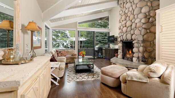 A spacious living room with a stone fireplace, a large window, and a cozy seating area. - Comfortable & Modern 2 Bedroom Apartments - Right on the Slopes! (Aspen)