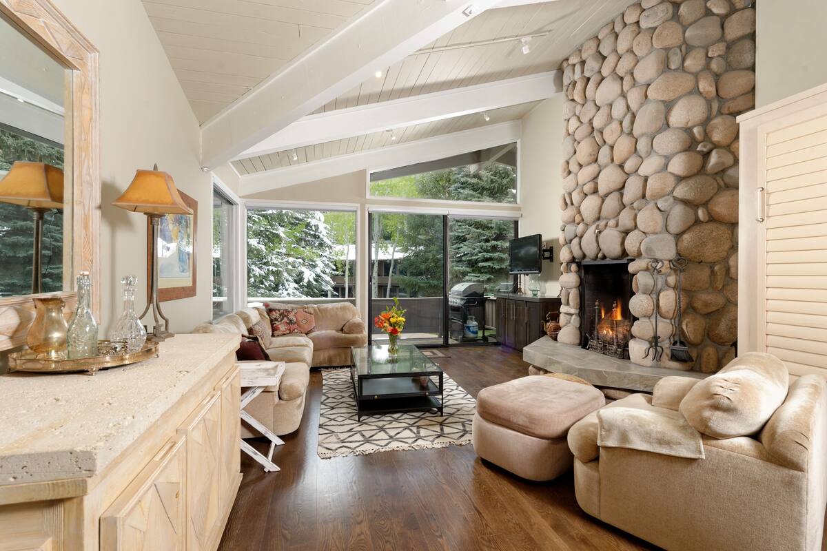 A spacious living room with a stone fireplace, a large window, and a cozy seating area.