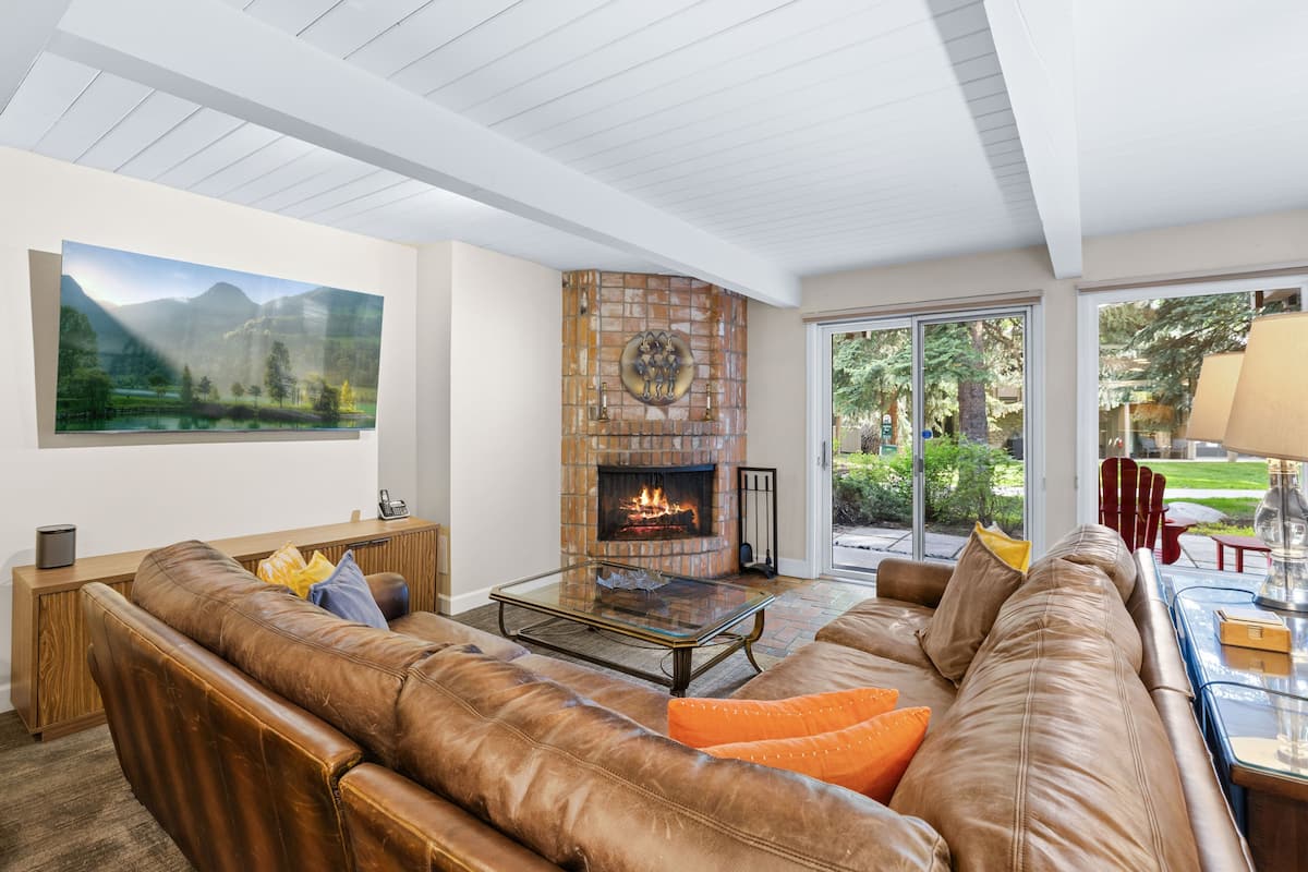 A living room with a leather sofa, a glass coffee table, a fireplace, and a large window.