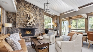 Una sala de estar acogedora con chimenea de piedra, sofás de cuero y un amplio ventanal con vistas al exterior.