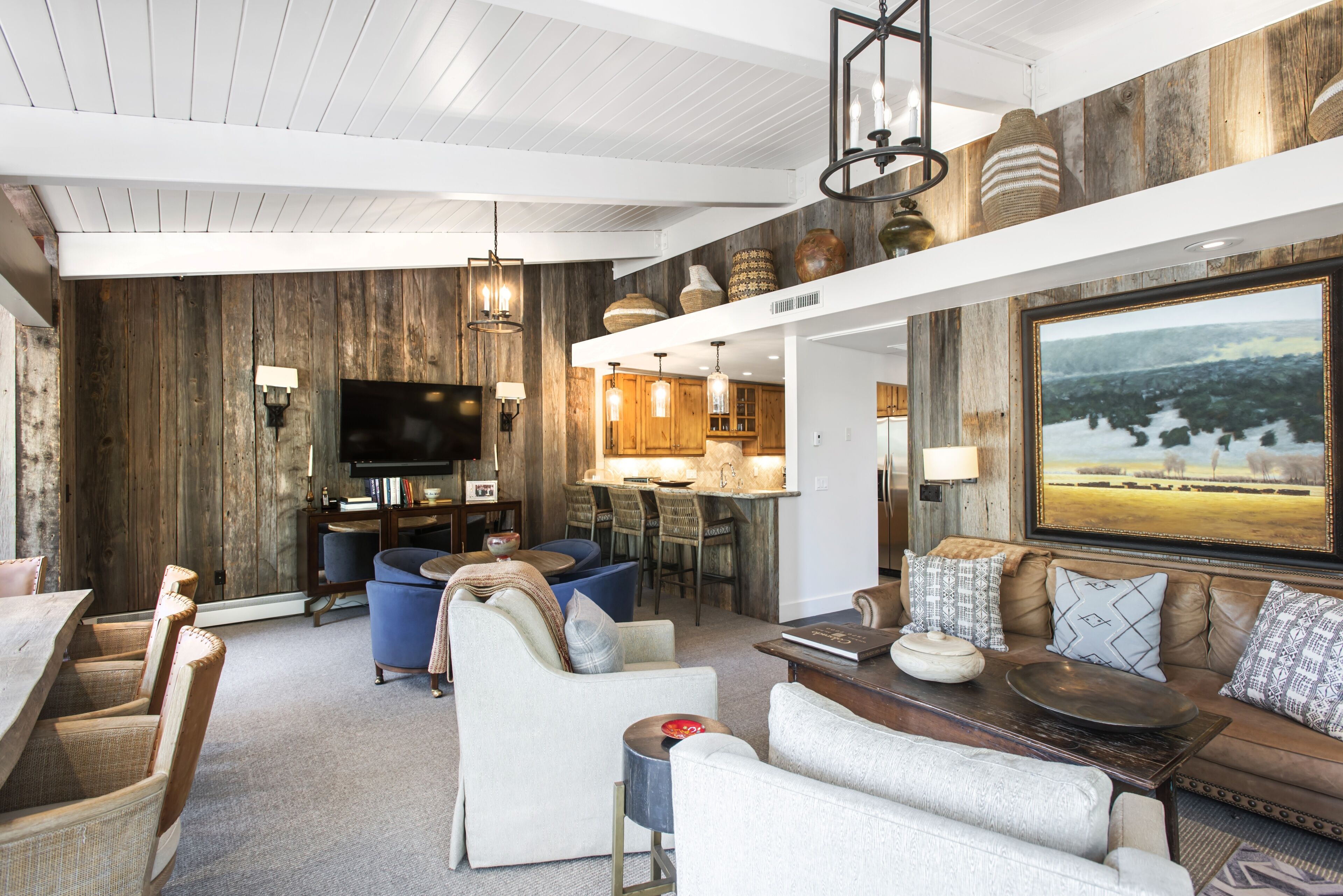 A modern living room with a wooden accent wall, a large flat-screen TV, and a dining area with a bar.