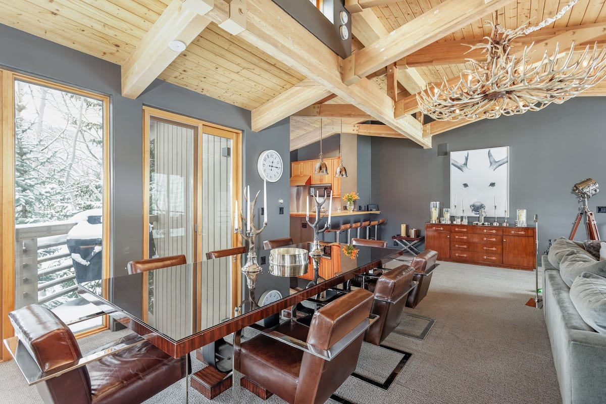 Een ruime woonruimte met een grote houten eettafel, omringd door lederen stoelen, een grijze bank en een houten kast.