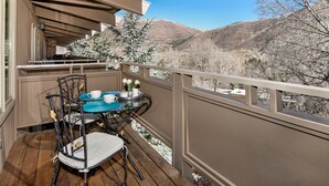A balcony with a table set for two, overlooking a mountainous landscape. - Two Bedroom Apartments with One of a Kind Location on Slopes of Aspen Mountain! (Aspen)