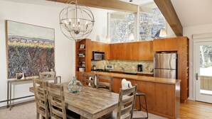 A modern kitchen with wooden cabinets, stainless steel appliances, and a dining area with a wooden table and chairs. - Two Bedroom Apartments with One of a Kind Location on Slopes of Aspen Mountain! (Aspen)