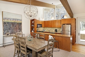 Eine moderne Küche mit Holzschränken, Edelstahlgeräten und einem Essbereich mit einem Holztisch und Stühlen.