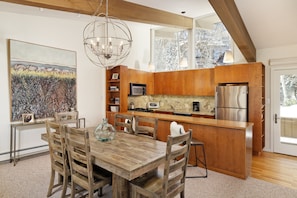 A modern kitchen with wooden cabinetry, a central island, and a dining area with a wooden table and chairs. - Two Bedroom Apartments with One of a Kind Location on Slopes of Aspen Mountain! (Aspen)