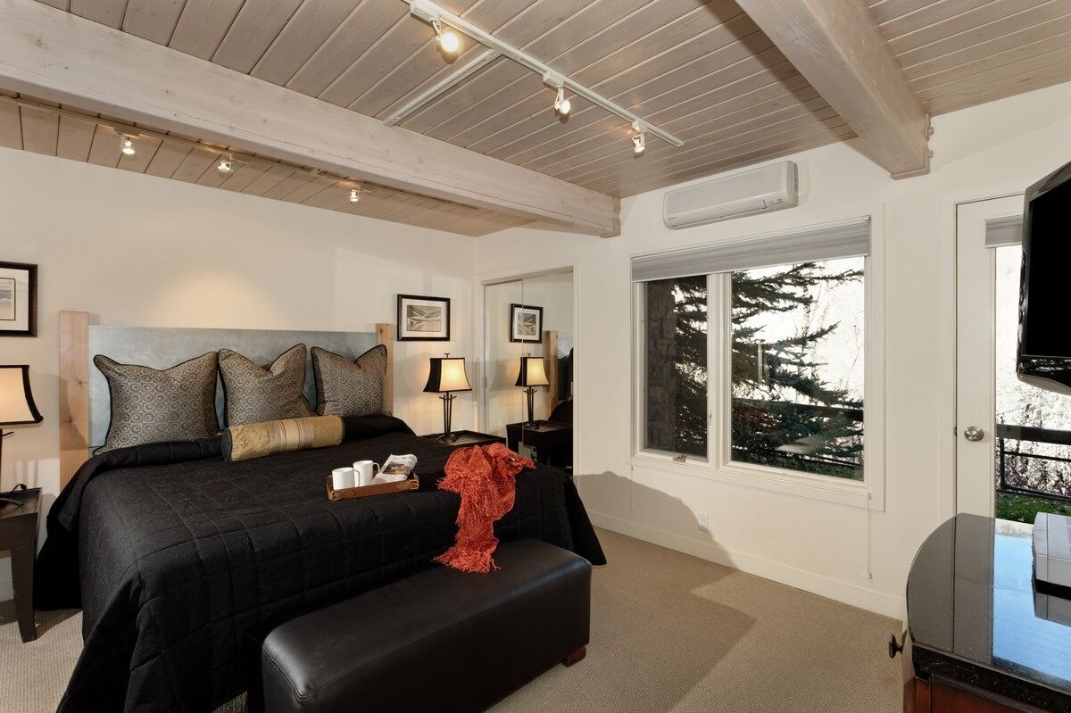 A bedroom with a large bed, bedside lamps, a window with a view of trees, and a television on a stand.