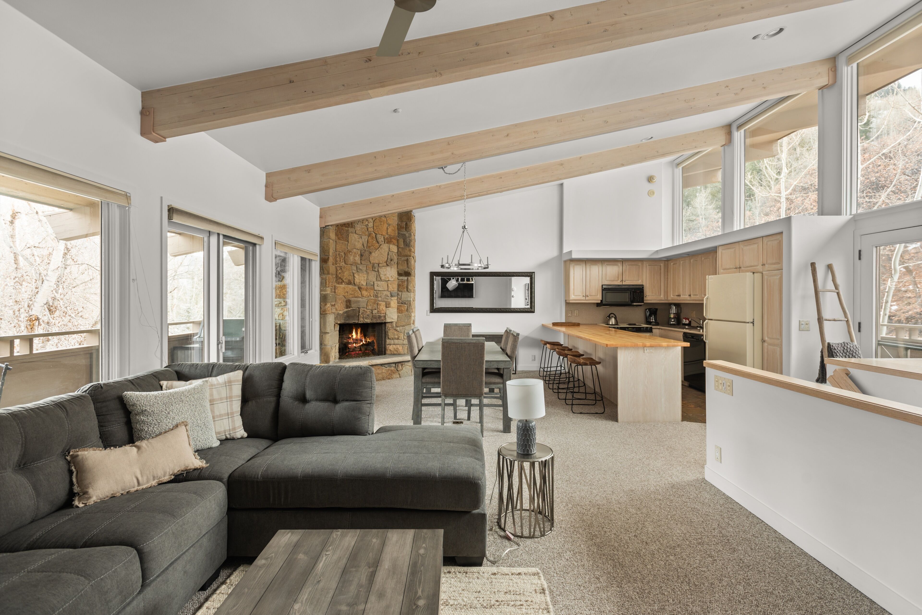 Una sala moderna con un sofá modular, comedor, cocina y ventanas amplias.