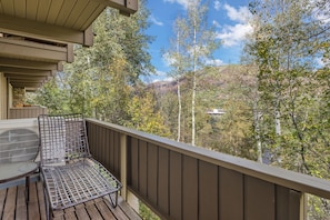 A balcony with a metal chair and a table, overlooking a forested area with mountains in the distance. - Aspen Alps Apartment #507 Home by RedAwning (Aspen)