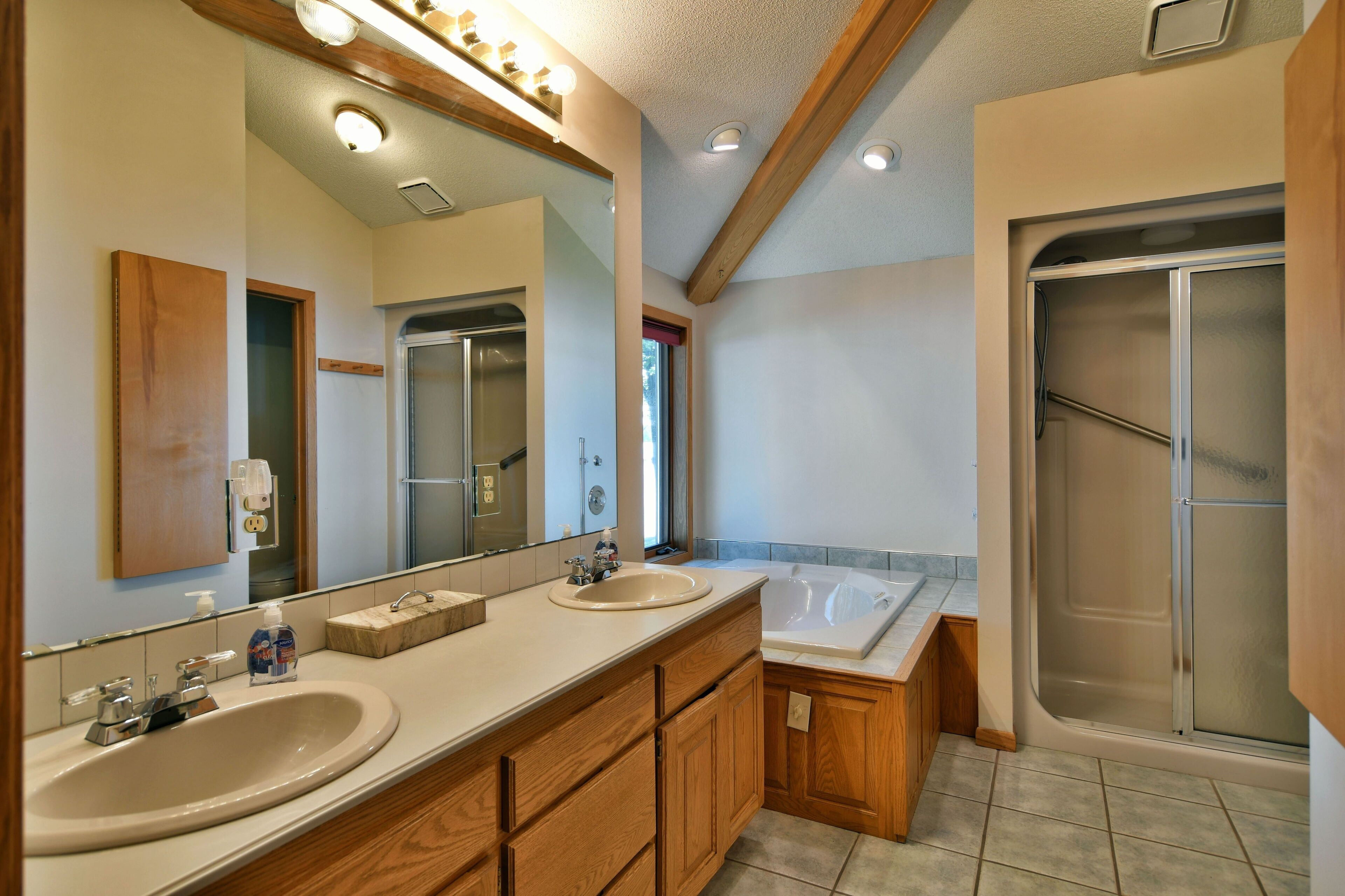 A modern bathroom with two sinks, a large mirror, wooden cabinetry, a bathtub, and a walk-in shower.