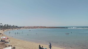 Una playa con gente nadando y tomando el sol.