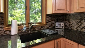 A kitchen with a black sink, wooden cabinets, a window with a view of trees, a paper towel holder, a soap dispenser, and a toaster. - Okemo Westwood Condo 3 Bedroom Condo by RedAwning (Ludlow)