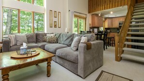A spacious living room with a grey sectional sofa, a wooden coffee table, and a staircase leading to a kitchen area. - Okemo Westwood Condo 3 Bedroom Condo by RedAwning (Ludlow)