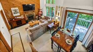 A cozy living room with a fireplace, a television, and a dining area with a table set for four. - Okemo Westwood Condo 3 Bedroom Condo by RedAwning (Ludlow)