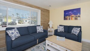 A living room with two dark blue sofas, a small white side table, a wooden coffee table, and a painting of a bridge at night on the wall.