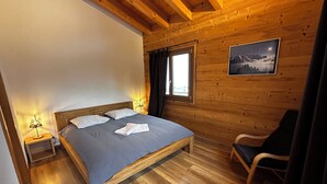 Un dormitorio de cabaña de madera con cama, lámpara de noche, silla y un cuadro enmarcado en la pared.