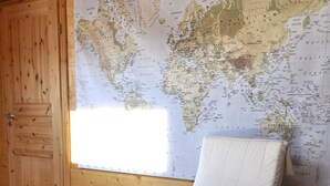 Interior de una cabaña de madera con un gran mapa del mundo en la pared, una silla de madera con cojín y un reposapiés a juego.
