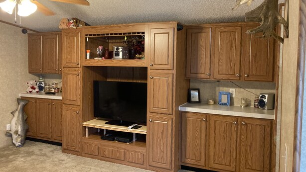 A kitchen with wooden cabinets, a ceiling fan, and a mounted fish sculpture. - Quiet secluded private single wide mobile home  (Jasper)