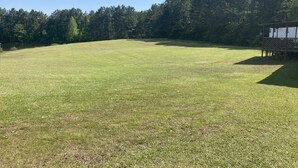 A grassy field with a wooden structure on the right, surrounded by trees. - Quiet secluded private single wide mobile home  (Jasper)