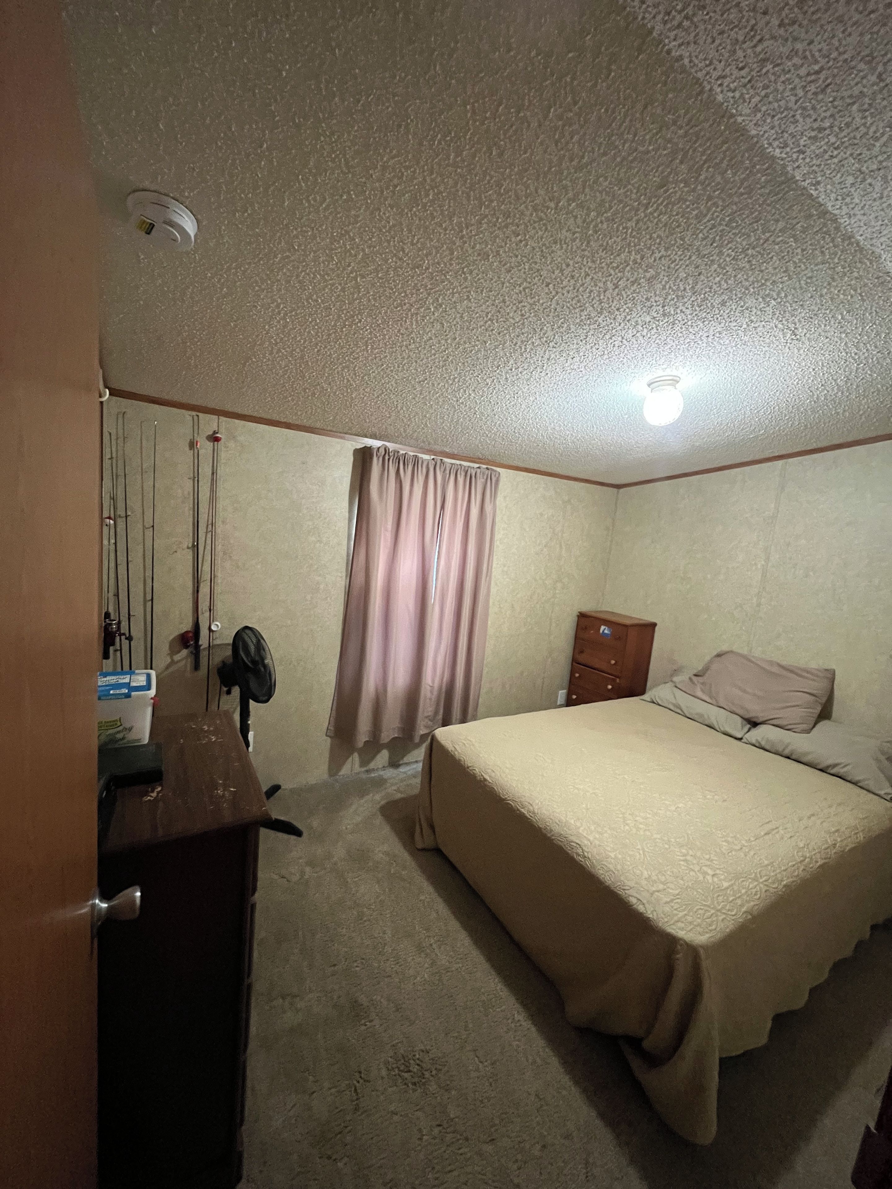 Une chambre à coucher avec un lit, une commode, un ventilateur de plafond et un rideau.