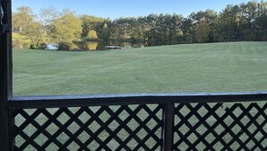 A view from a covered area with a wooden lattice fence, overlooking a well-maintained grassy field and a body of water, with trees in the background. - Quiet secluded private single wide mobile home  (Jasper)